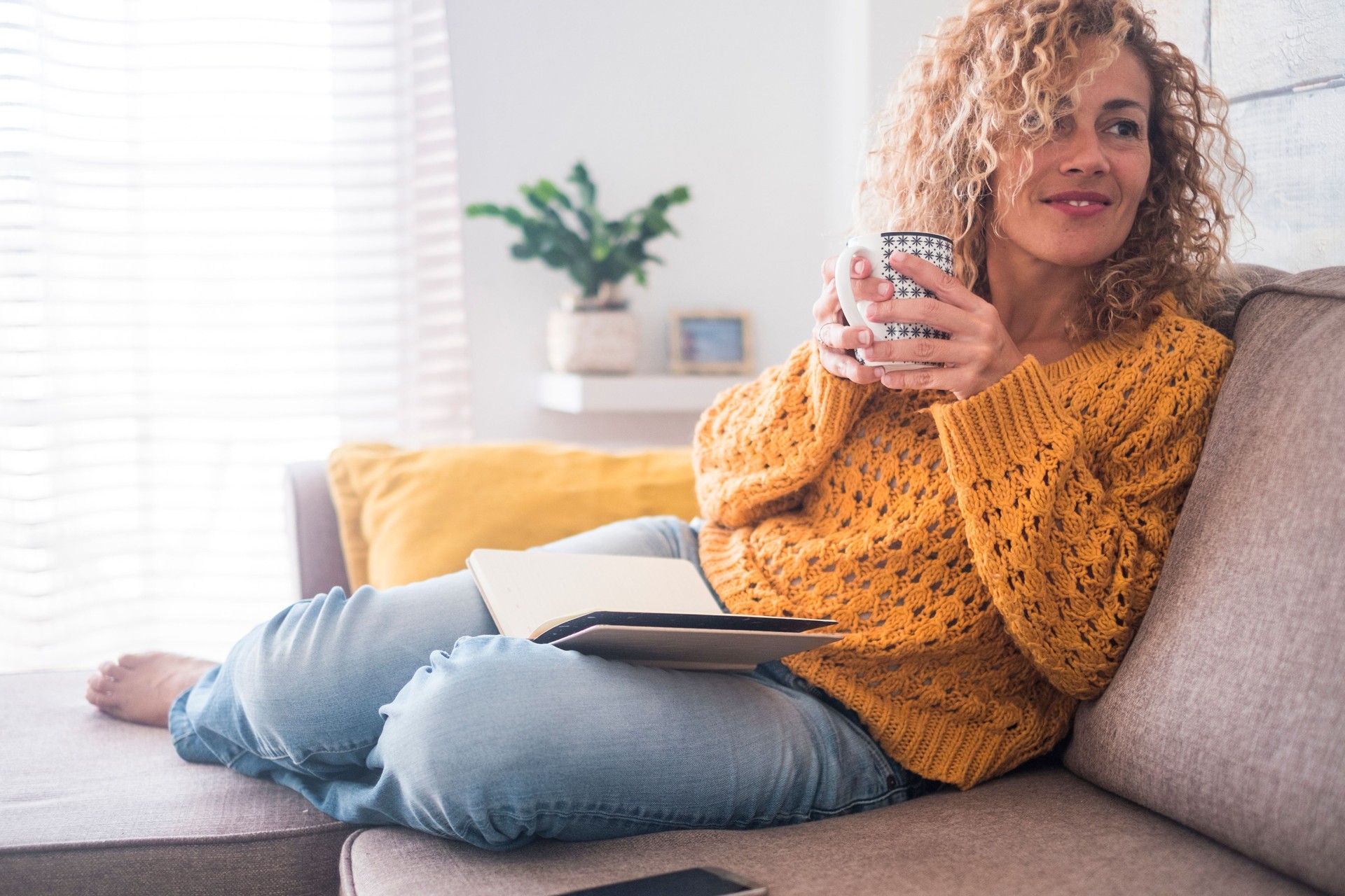 Hermosa de 40 años caucásico señora Siéntese en el sofá bebiendo té y leyendo un libro para la actividad de ocio interior por la tarde en casa - después de estilo de vida de trabajo para el concepto de personas